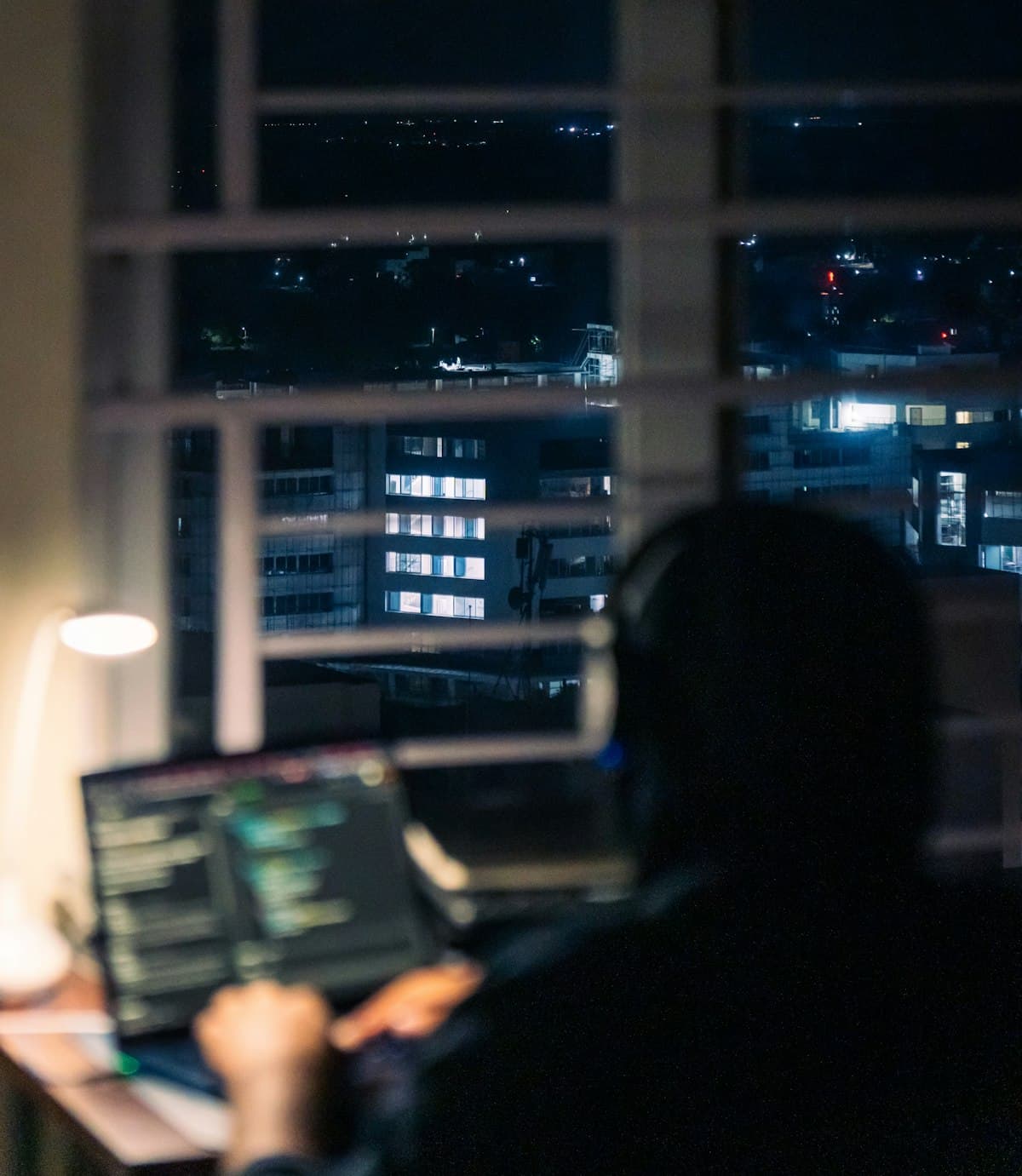 Person working on a laptop at night overlooking city buildings